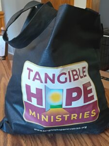 Black Reusable Grocery Bag with the Tangible Hope Logo, stuffed with hygene items for Living Forward Participants